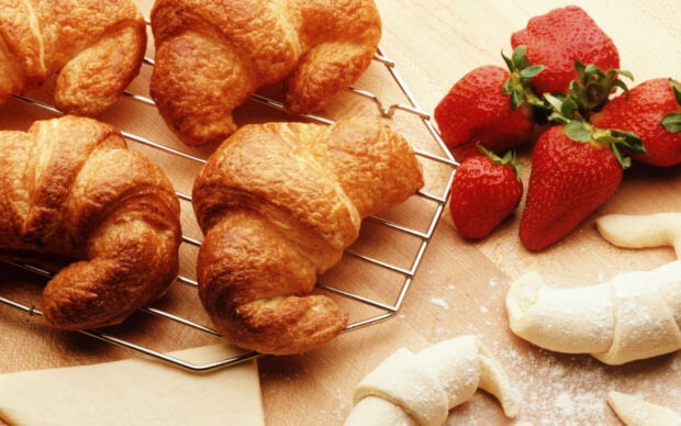 Freshly baked croissant with raw croissant dough and ripe strawberries on a wooden surface