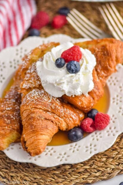 Delicious croissant topped with whipped cream and fresh berries on a decorative plate
