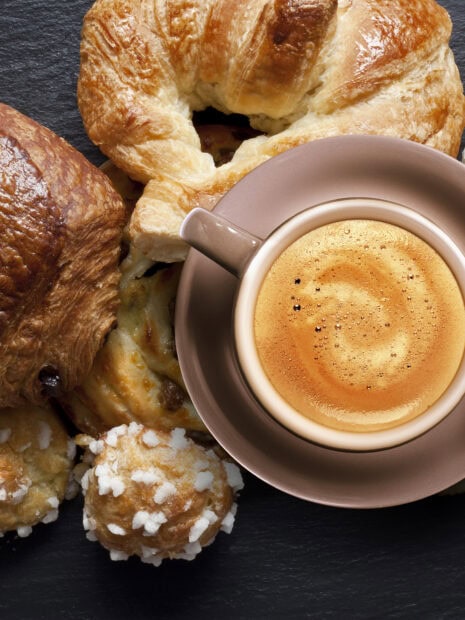A close up of croissant and pastries next to a cup of coffee on a dark surface