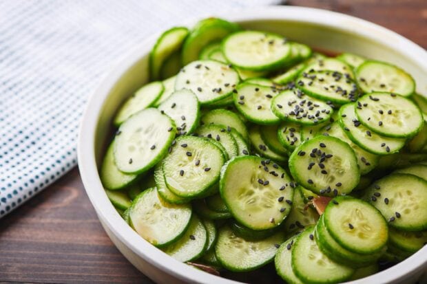 Fresh cucumber slices garnished with black sesame seeds in a white bowl