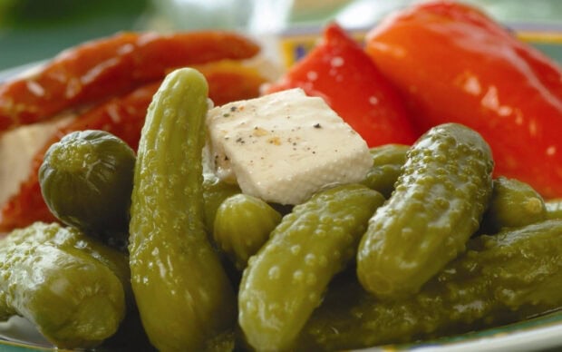 A close up of cucumbers with a piece of seasoned cheese surrounded by red peppers
