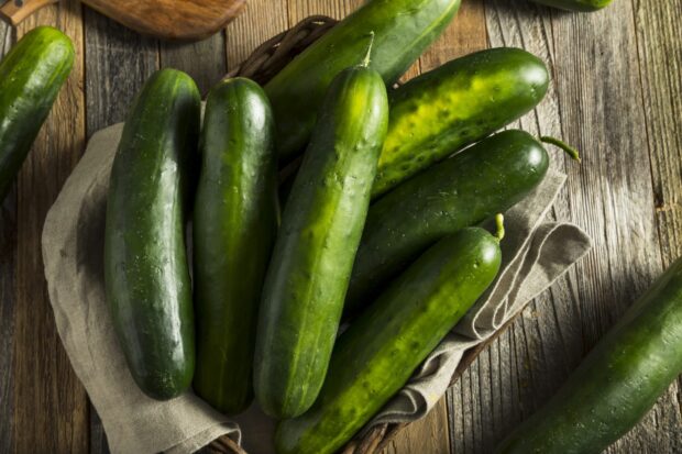 Fresh green cucumbers arranged in a basket on a wooden surface with a cloth lining