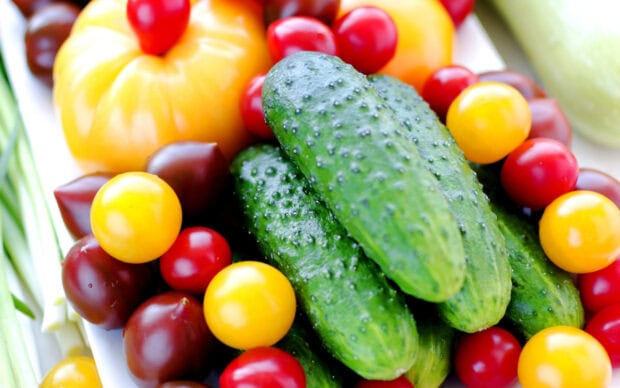 Fresh green cucumbers surrounded by colorful cherry tomatoes and yellow tomatoes on a white surface