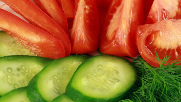 Fresh cucumber slices arranged with red tomatoes and dill herbs on a plate