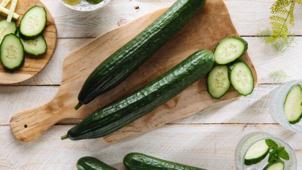Fresh cucumber slices and whole cucumbers arranged on a wooden board and table for a healthy snack