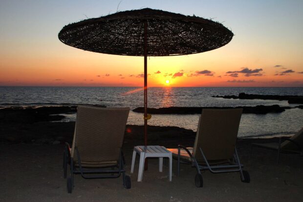 Two chairs under an umbrella overlooking the Cyprus sunset over the sea