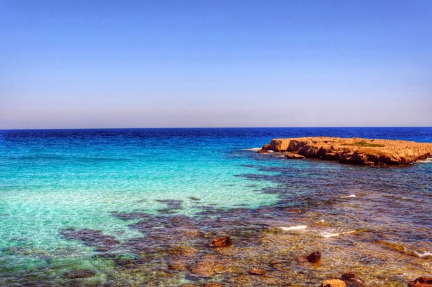 Clear turquoise water near rocky coast of Cyprus with bright blue sky