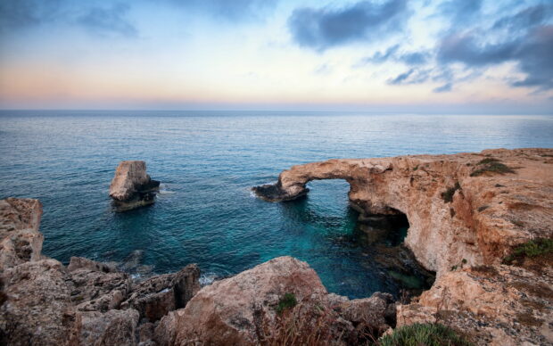 Natural rock arch formation by the sea in Cyprus with clear blue water and rocky cliffs