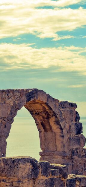 Ancient ruins arch from Cyprus near calm sea and cloudy sky in the background