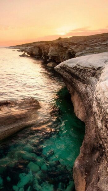 Clear turquoise water meets rocky shorelines in Cyprus during a golden sunset