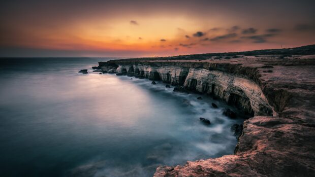 Natural cliff formations in Cyprus coastline at sunset with calm sea and colorful sky