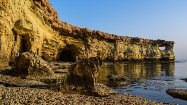Natural rock formations of Cyprus coastline with caves and clear water at sunset