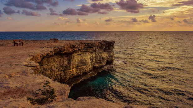 Rocky coast of Cyprus with sea and sunset clouds in warm light