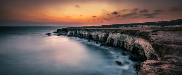 Rocky coastline of Cyprus and calm sea under sunset sky