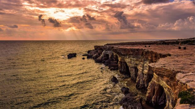Stunning Cyprus coastline with rocky cliffs under a dramatic cloudy sky at sunset
