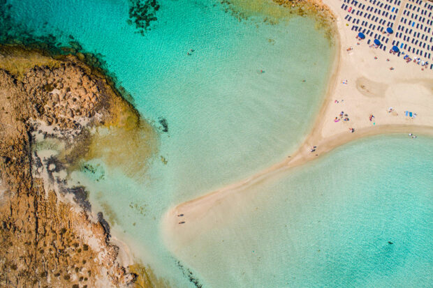 Aerial view of Cyprus crystal clear turquoise water and sandy coast with people relaxing on the beach