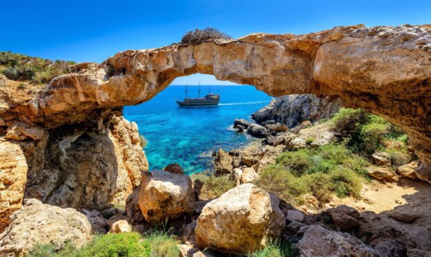 Natural rock arch and turquoise sea with a ship in Cyprus coast scenery