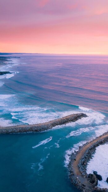 A beautiful coast of Cyprus with vibrant waters and a boat near the rocky breakwater under a colorful sky