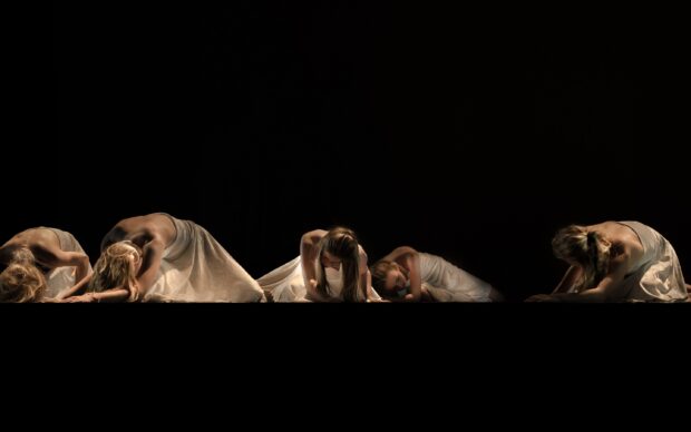 Contemporary dancers performing floor movements in elegant dresses on a dark stage