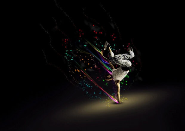 A breakdancer performing a handstand with colorful light trails and particles surrounding the dancer