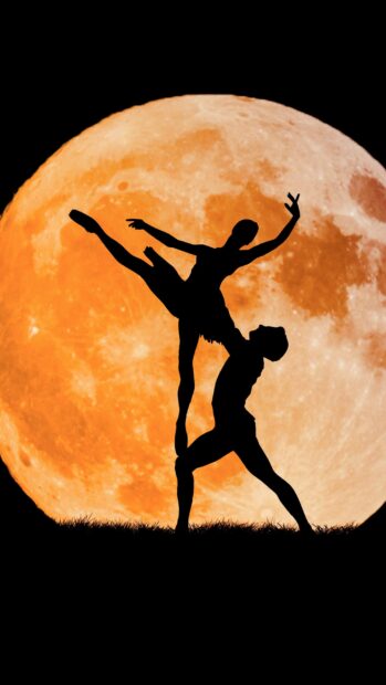 Silhouette of dancers performing a ballet pose in front of a large full moon