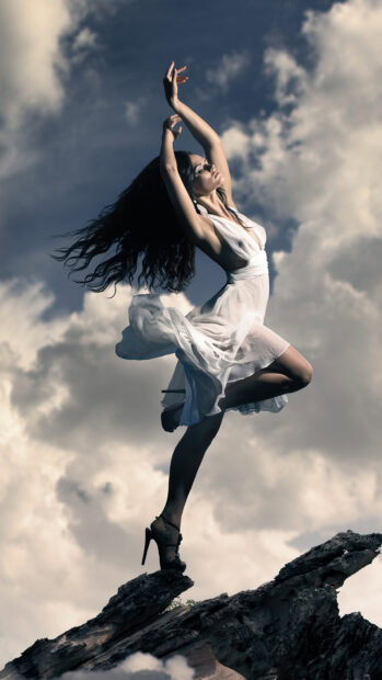 Graceful dancer posing on rocky edge with flowing dress and dynamic movement