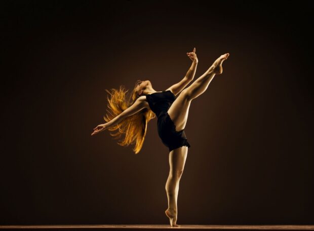 A dancer performing an elegant high kick with flowing hair in a black outfit