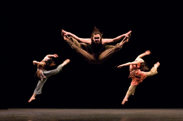 A group of dancer performing high jumps in a dark theater with focused expressions