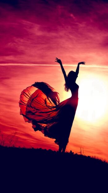 Silhouette of a dancer gracefully moving with flowing dress against a vibrant sunset sky