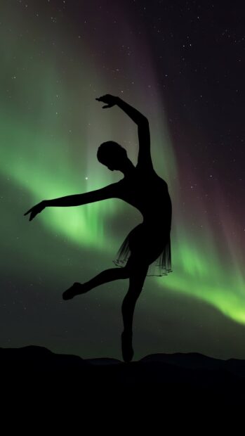 Silhouette of dancer performing ballet pose in front of northern lights display