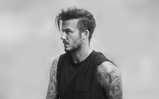 David Beckham with tattoos on arms and styled hair looking sideways in a black sleeveless shirt