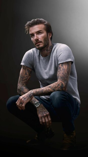 David Beckham with tattoos wearing a grey t shirt and jeans crouching thoughtfully