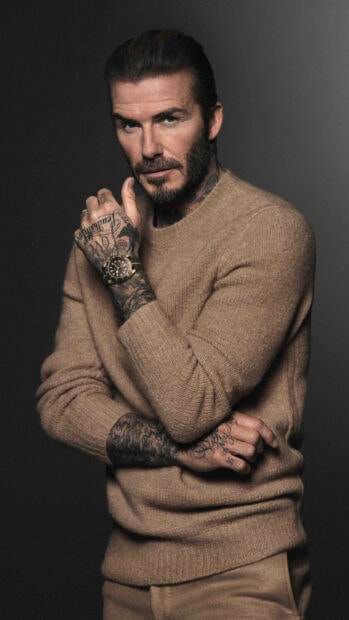 David Beckham with tattoos wearing a brown sweater and watch looking intensely