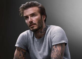 David Beckham with tattoos and beard posing in a grey t shirt with a serious expression