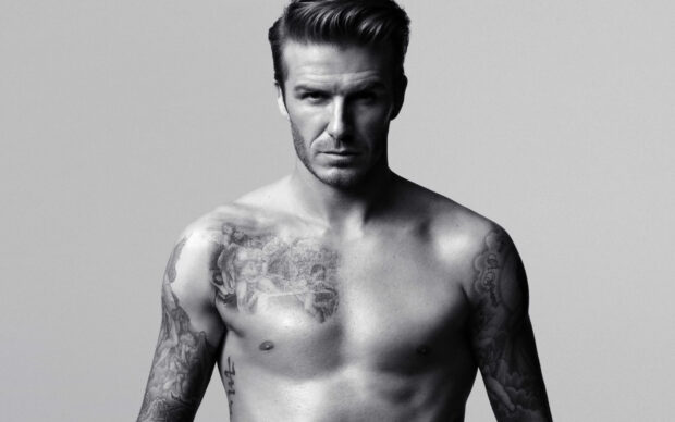 David Beckham shirtless with tattoos on both arms and chest in black and white portrait
