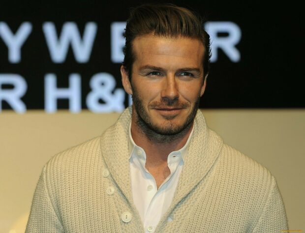 David Beckham wearing a white shirt and knitted sweater with a slight smile on his face