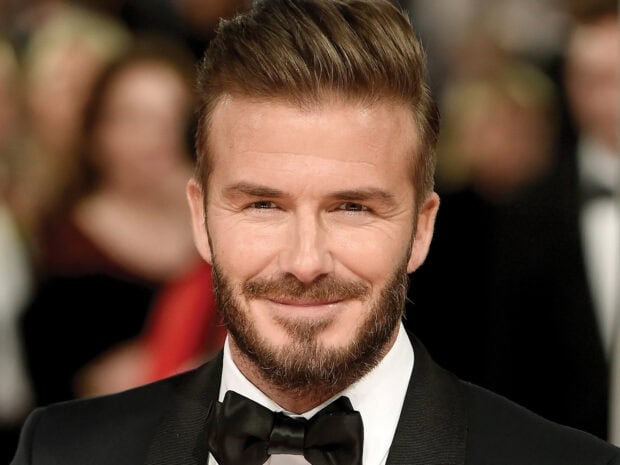 David Beckham smiling in a tuxedo at a formal event with facial hair and styled hair