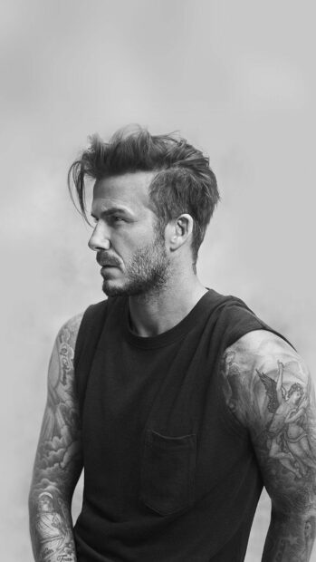 David Beckham with tattooed arms wearing a black sleeveless shirt looking to the side in black and white