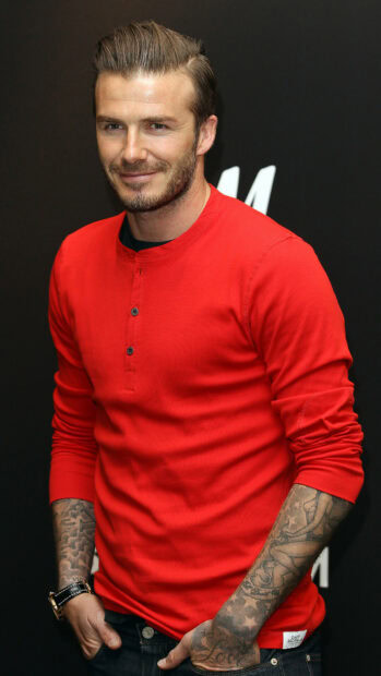 David Beckham wearing a red shirt showing his tattoos and smiling confidently