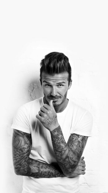 David Beckham with tattooed arms wearing a white t shirt posing thoughtfully