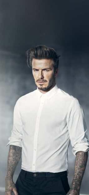 David Beckham with tattoos and styled hair wearing a white shirt and black pants