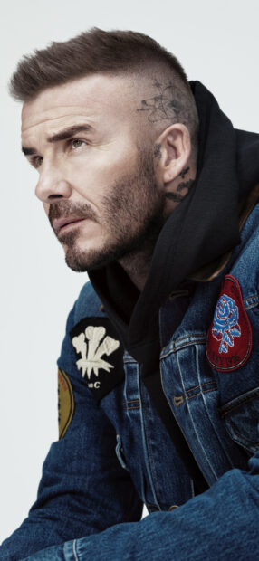 David Beckham with unique tattoos wearing a denim jacket looking thoughtfully to the side