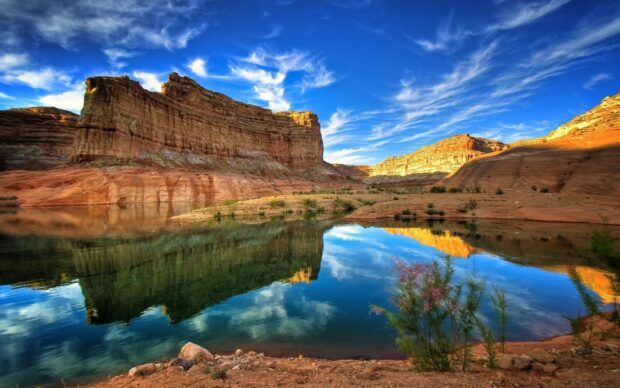 Red rock formations in Denver Colorado reflecting on calm water under a bright blue sky with scattered clouds