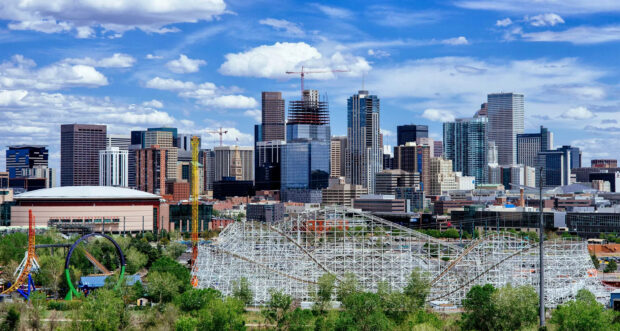 Denver city skyline with roller coaster and construction cranes under a blue sky with clouds
