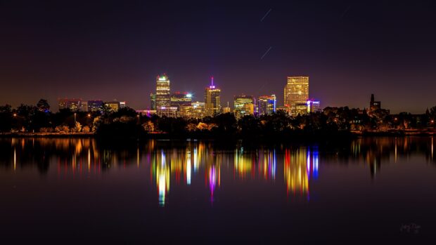 The Denver city skyline at night reflecting colorful lights on the calm water surface