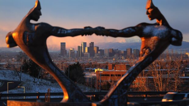 The Denver city skyline framed by a metal sculpture of two figures holding hands at sunset