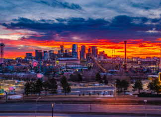 Denver skyline lit up against a vibrant sunset sky with city buildings and amusement park rides visible