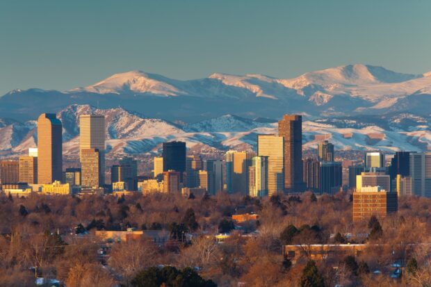 A clear view of Denver skyline surrounded by snow covered mountains in winter sunlight