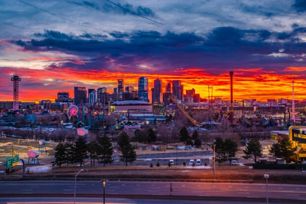 Denver skyline lit up against a vibrant sunset sky with city buildings and amusement park rides visible