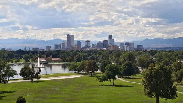 A scenic view of Denver skyline with lush green park and fountain in the foreground